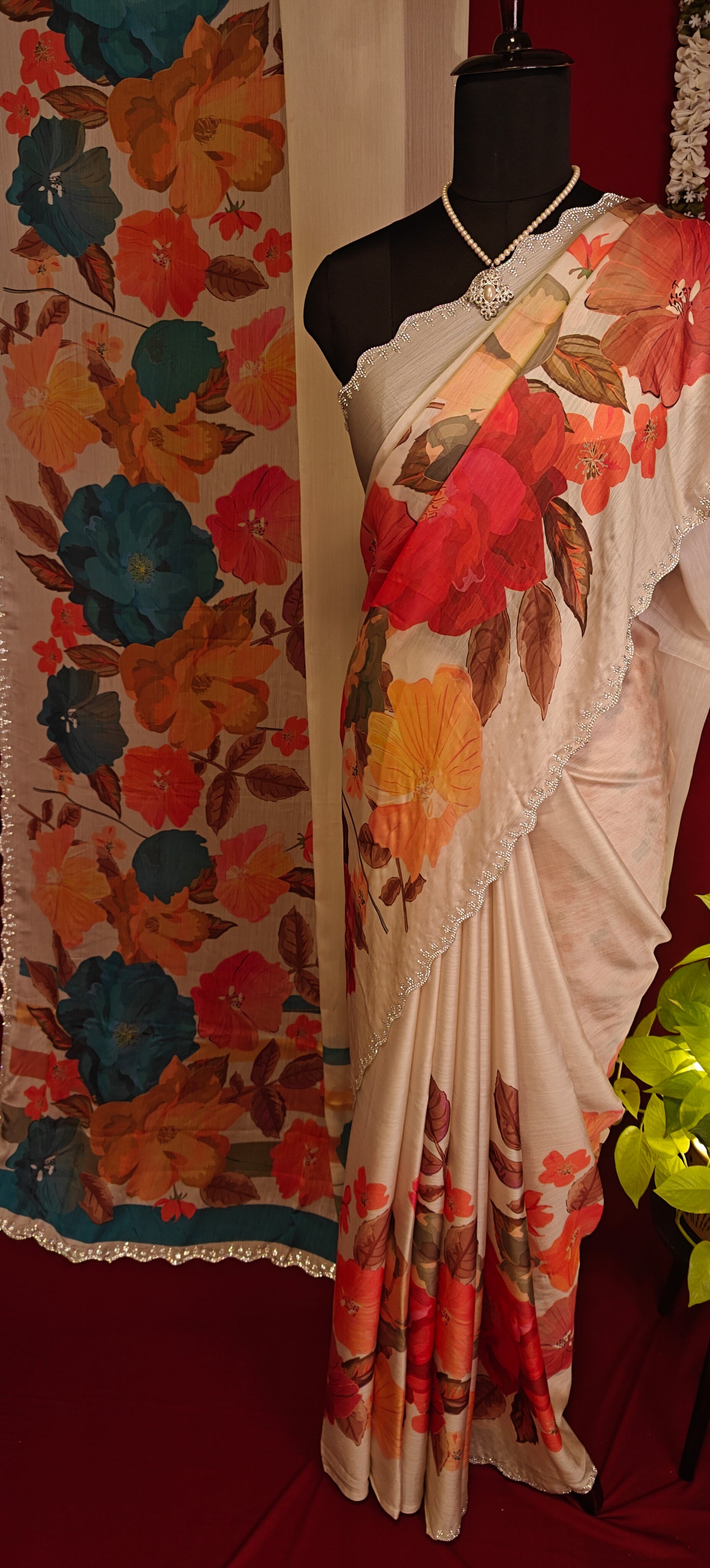 Cream satin chiffon saree with orange floral print and silver scalloped border and decorative items in the background.