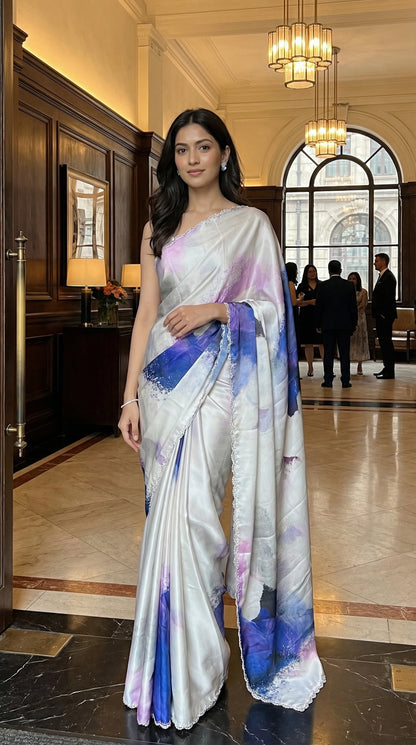 White satin georgette saree with abstract blue brushstroke print and scalloped border, in an elegant indoor setting.