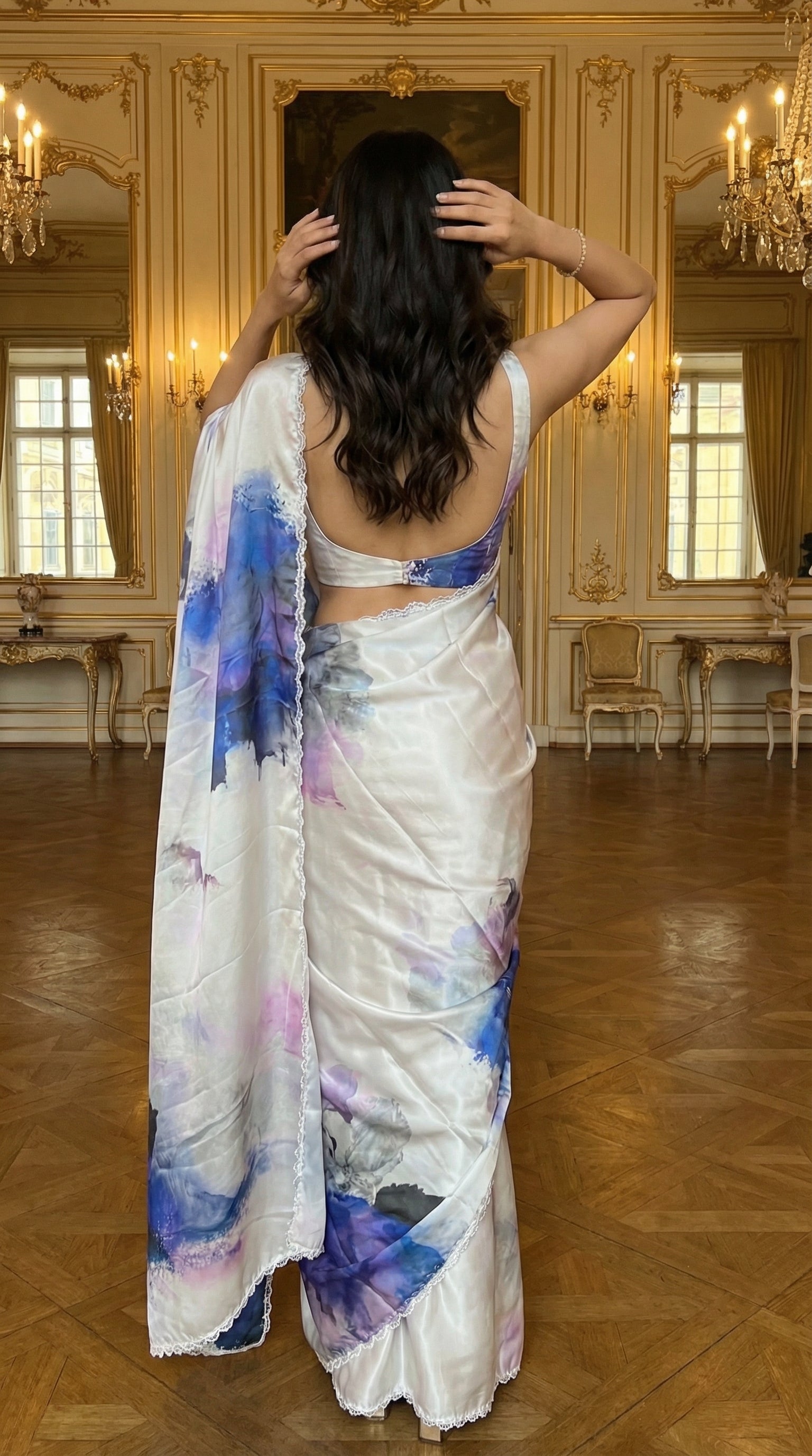 White satin georgette saree with abstract blue brushstroke print and scalloped border, in an elegant room.