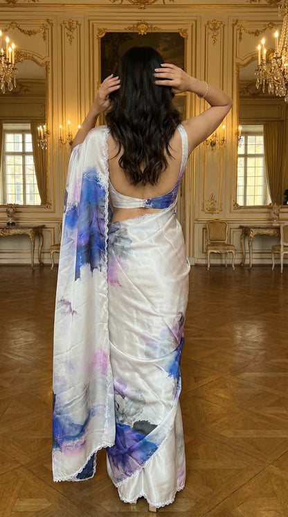White satin georgette saree with abstract blue brushstroke print and scalloped border, in an elegant room.
