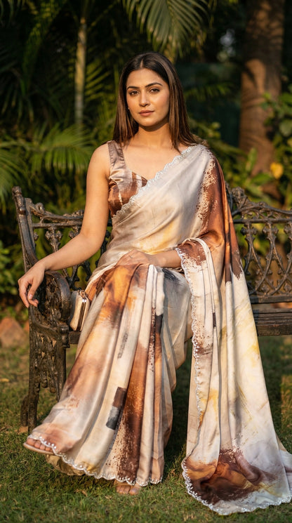 White satin georgette saree with abstract brown brushstroke print and scalloped border, sitting outdoors with greenery in the background.
