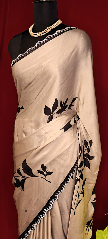 Cream satin georgette saree with medium-sized black leaf print, black motif border, and matching blouse piece on a mannequin against a red background