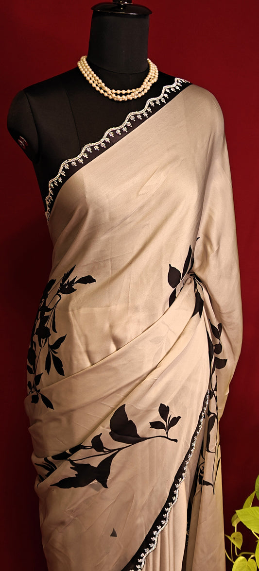 Cream satin georgette saree with medium-sized black leaf print, black motif border, and matching blouse piece on a mannequin against a red background