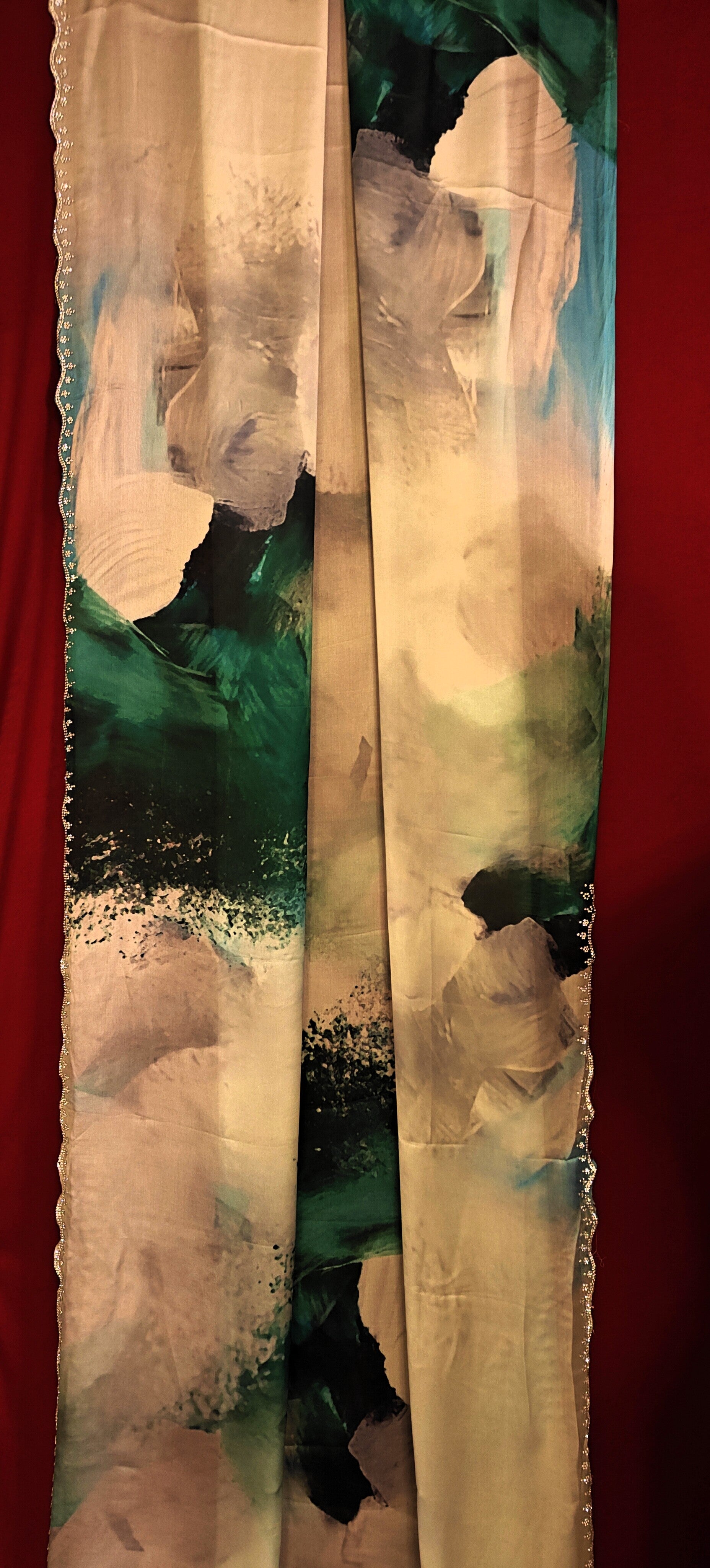 White satin georgette saree with abstract green brushstroke print and scalloped border hanged against a red background.