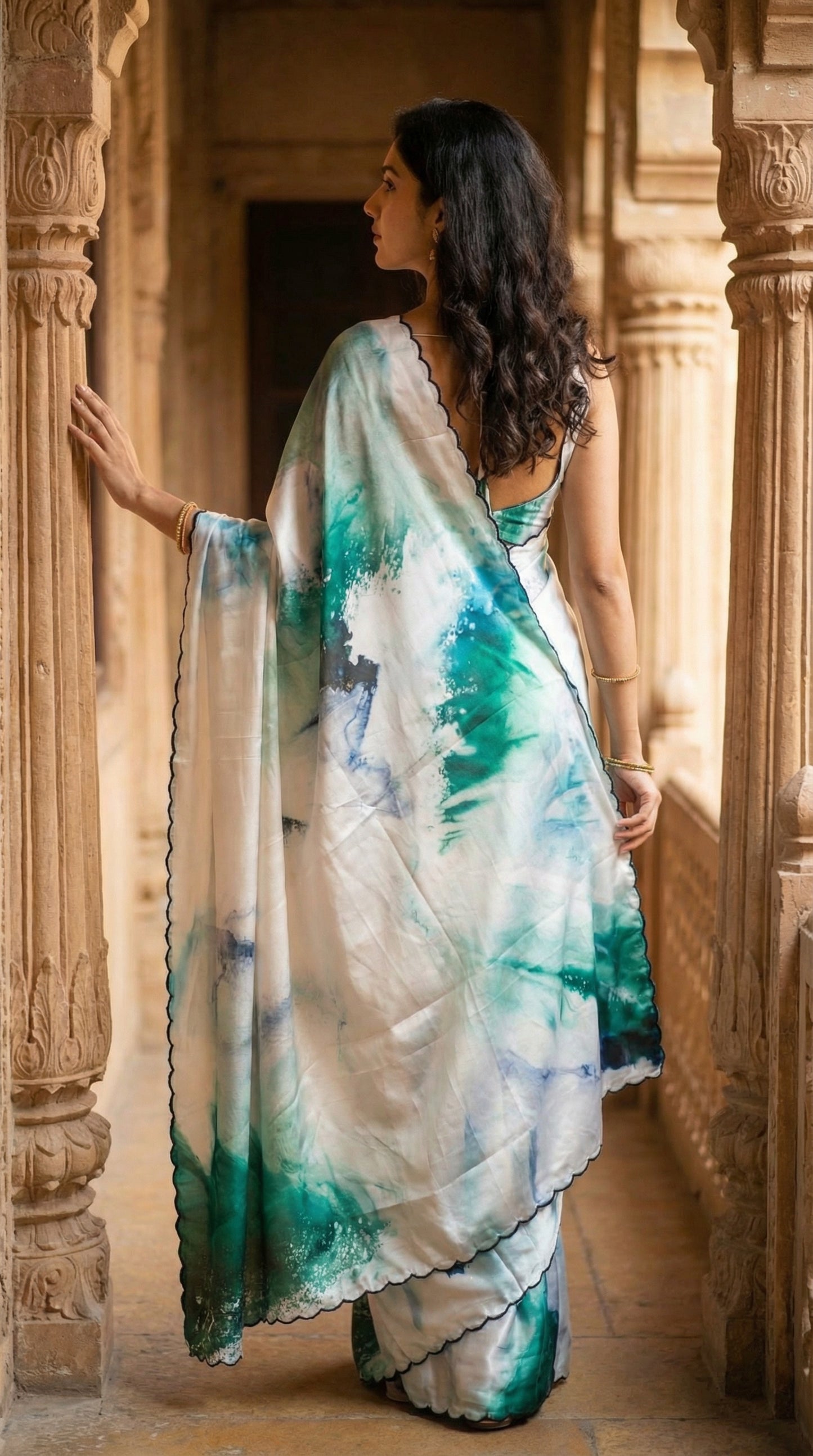 White satin georgette saree with abstract green brushstroke print and scalloped border, in an architectural setting.