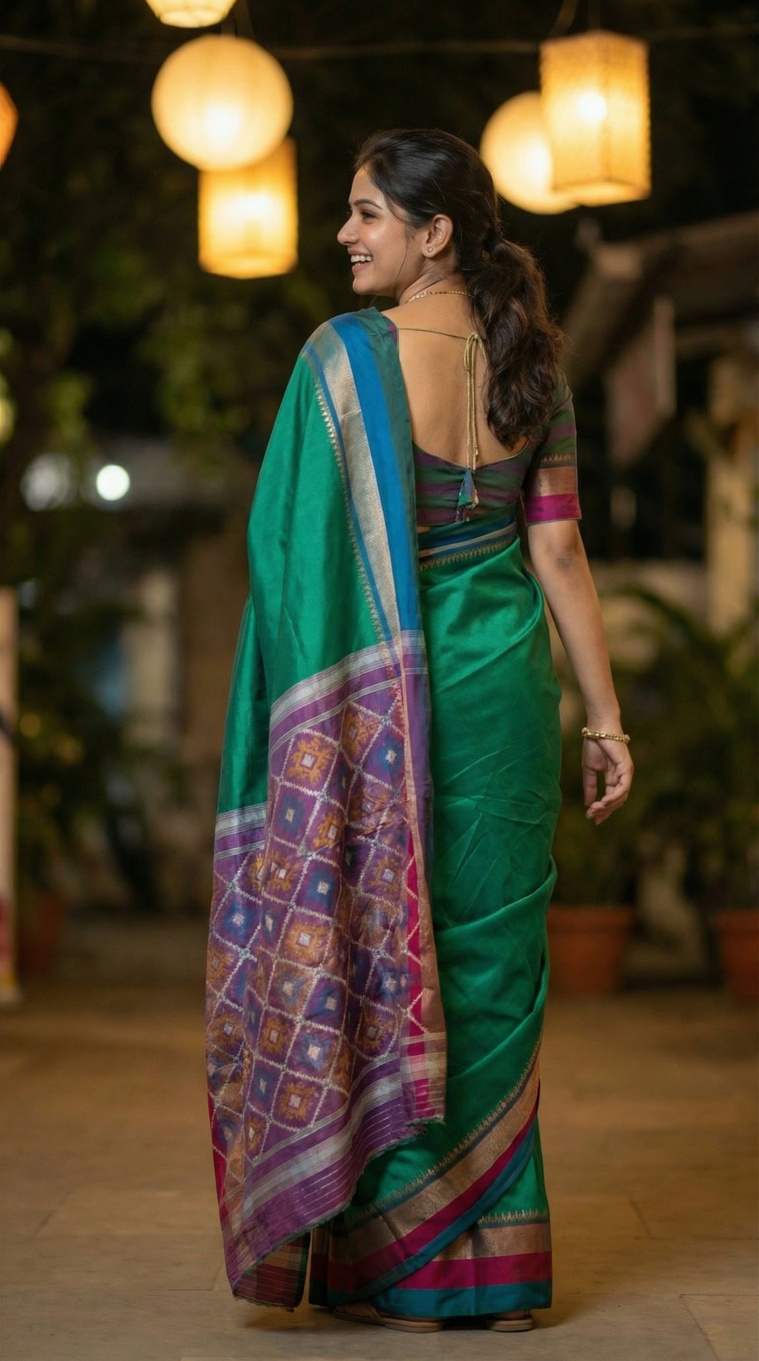 Woman in a soft silk saree in peacock green with multicolor border and dotted digital print, standing outdoors near her house.