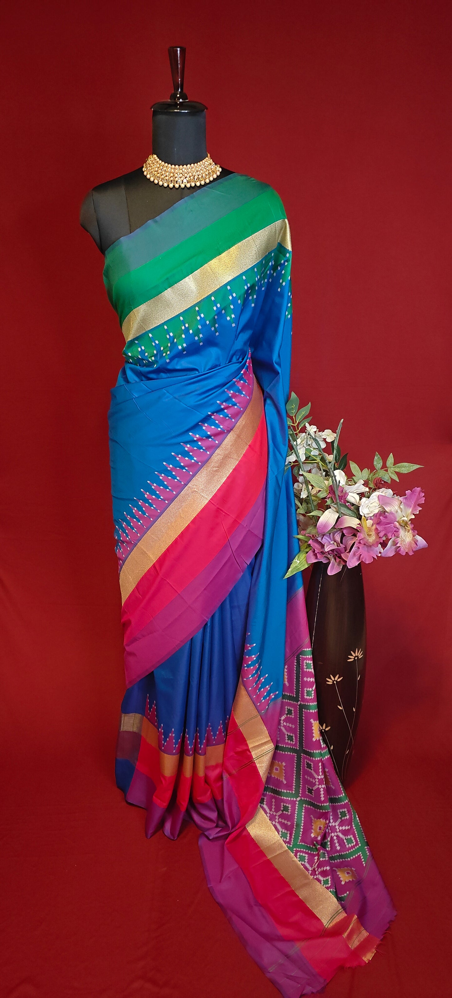 soft silk saree in sapphire blue with multicolor border and dotted digital print, styled on mannequin with flower vase against red background.