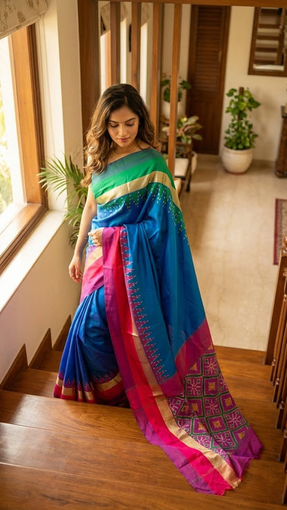 Woman wearing a soft silk saree in sapphire blue with multicolor border and dotted digital print indoors with wooden flooring and plants in the background.
