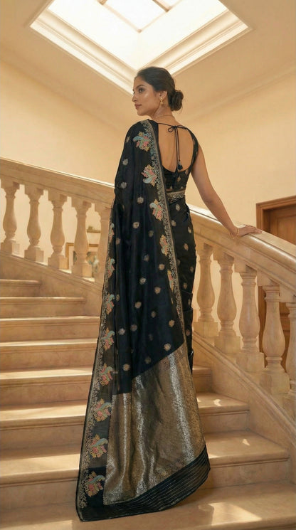 Woman in a Black Silk Saree with Zari Embroidery with parrot motifs, standing on a staircase.