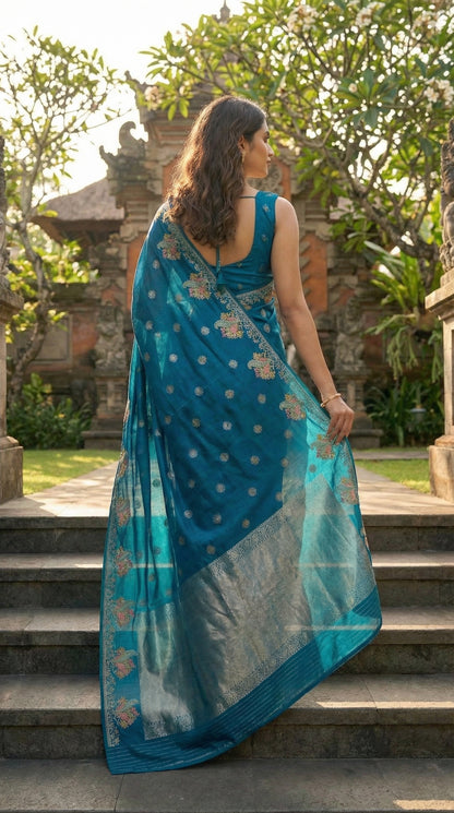Woman in a Blue Silk Saree with Zari Embroidery with parrot motifs, standing on steps with a temple-like structure in the background.