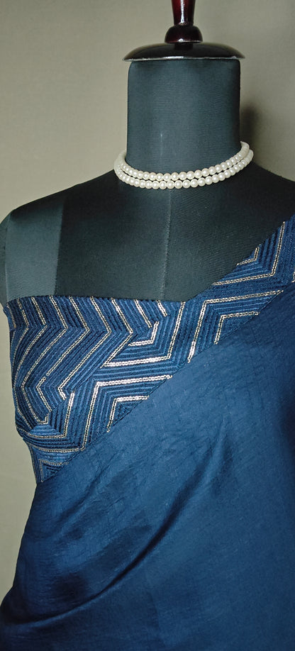Blue silk saree with metallic zigzag border in gold and silver, displayed on mannequin with pearl necklace.