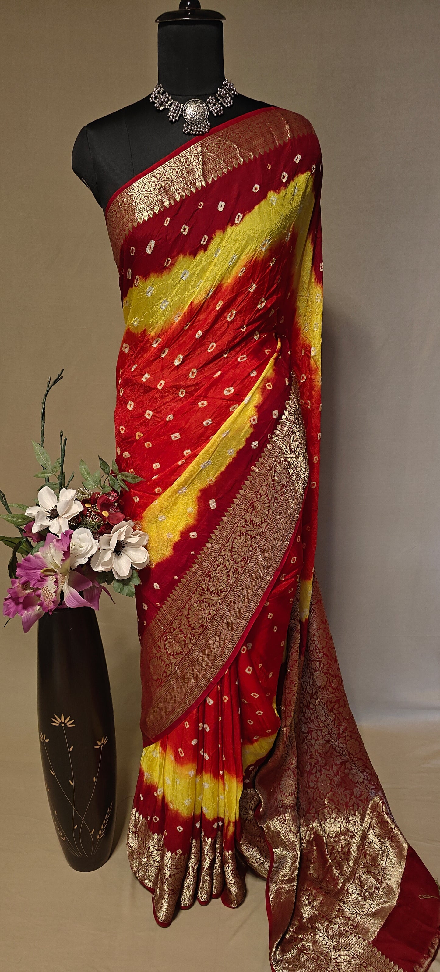 Red and yellow silk saree with floral arrangement on a mannequin against a neutral background.