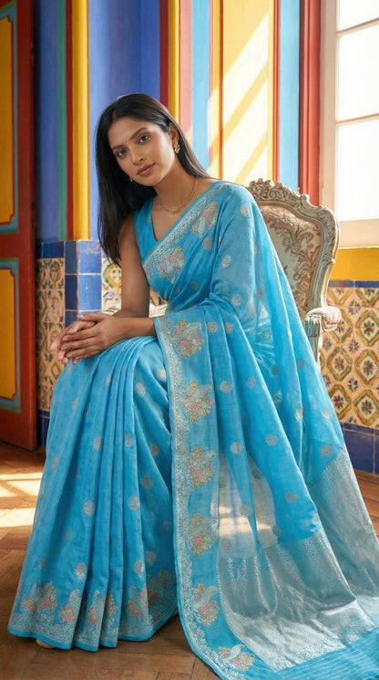 Woman in a Sky Blue Silk Saree with Zari Embroidery with parrot motifs, with a colorful background.