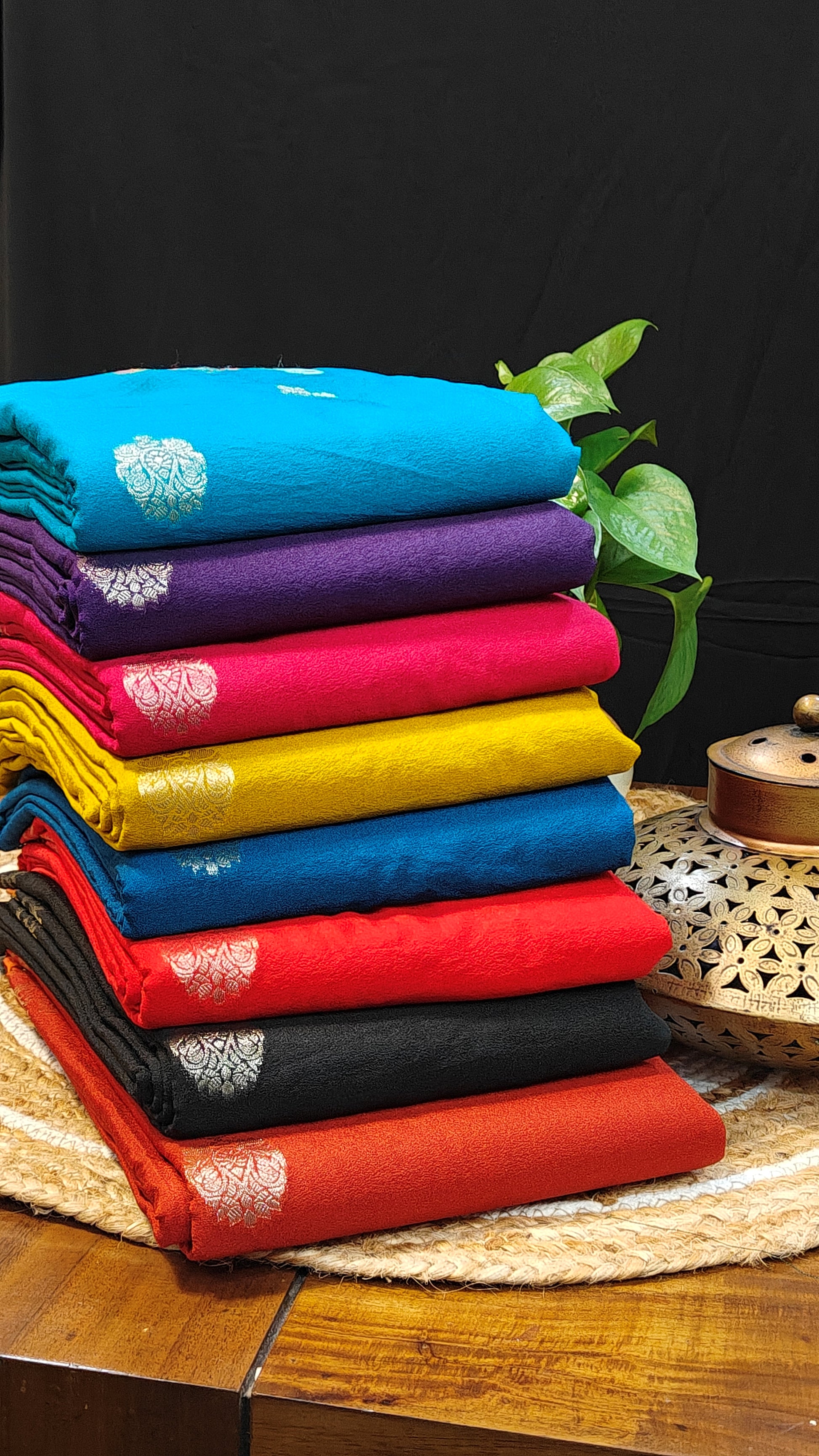 Silk Saree with Zari Embroidery with parrot motifs in eight colors stacked up one above another on a wooden table.