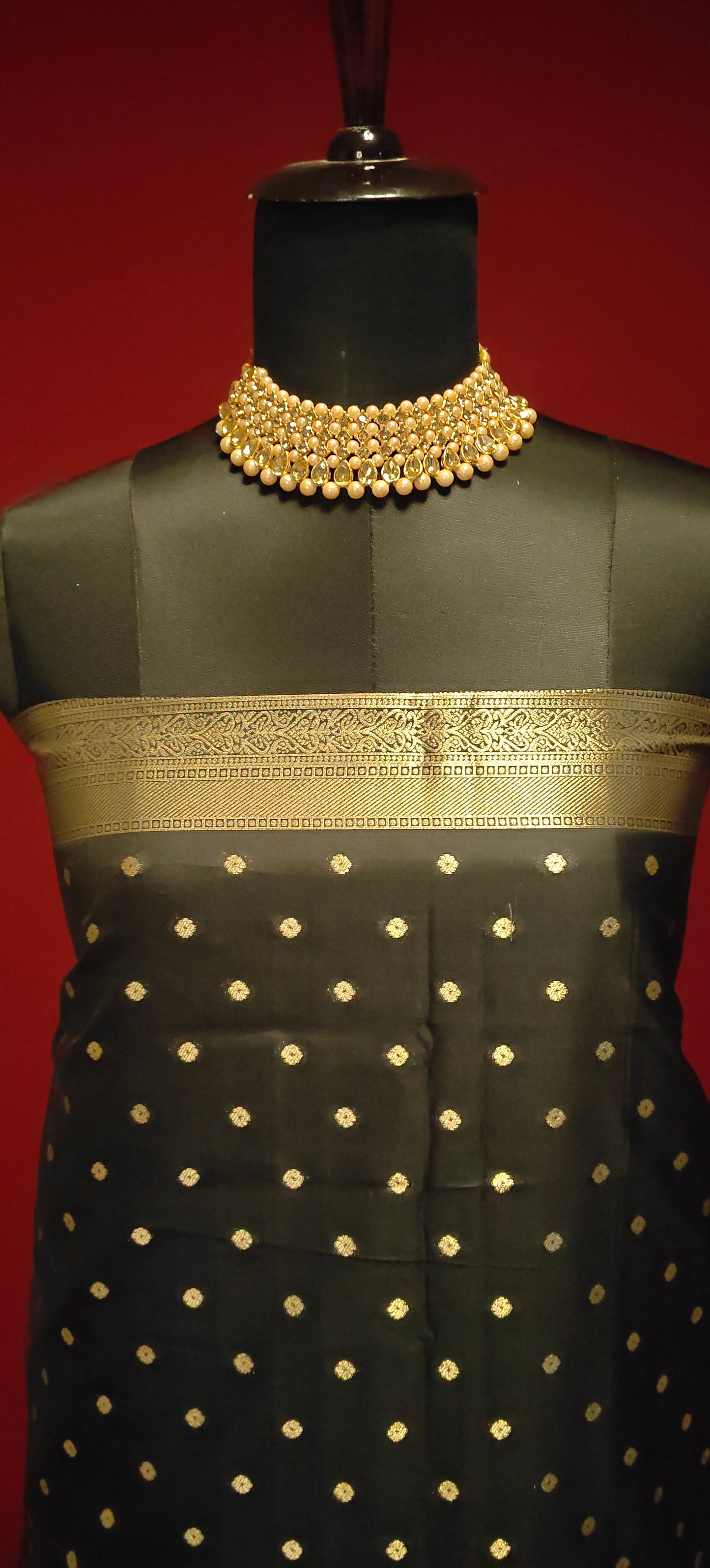 Black soft silk saree with gold and silver floral motifs and rich zari border draped on mannequin showcasing the blouse piece against a red background.