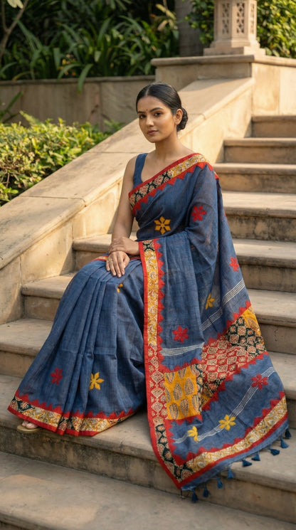 Woman in a slate grey linen cotton saree with traditional applique border, sitting on steps outdoors.
