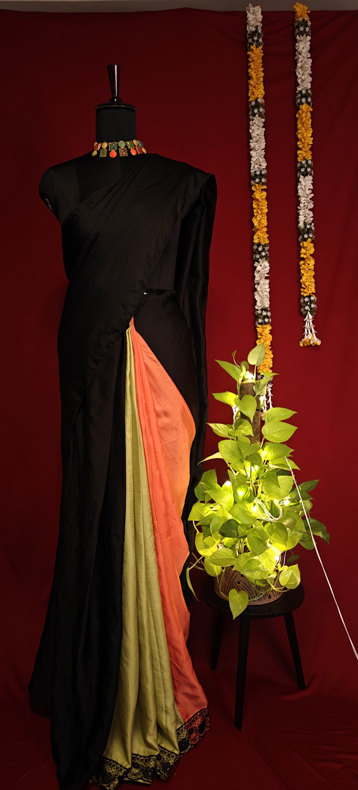 Black strawberry silk saree with soft sheen and elegant drape, styled on mannequin with decorative items against a red background.