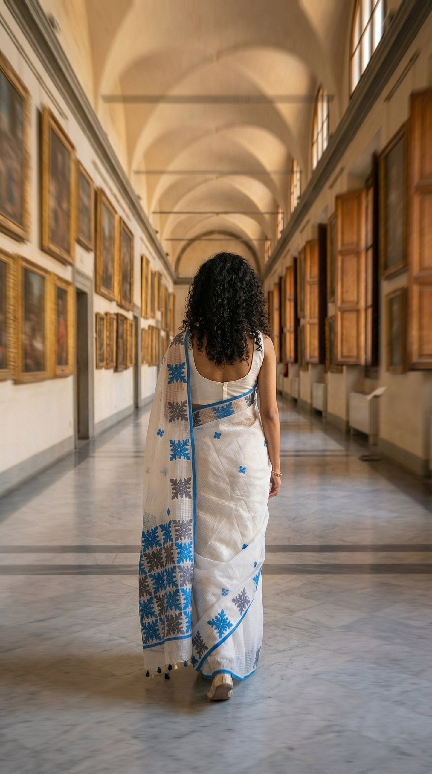 Woman in a white-blue-grey-applique-kota-saree, walking through an art gallery.