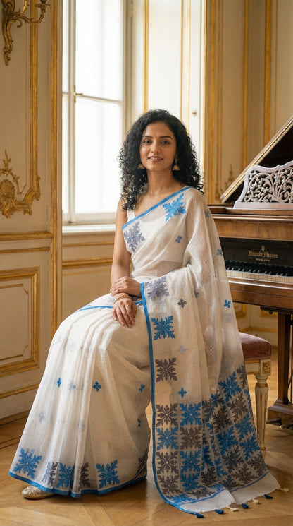 Woman in a white-blue-grey-applique-kota-saree, sitting in a room with a piano.