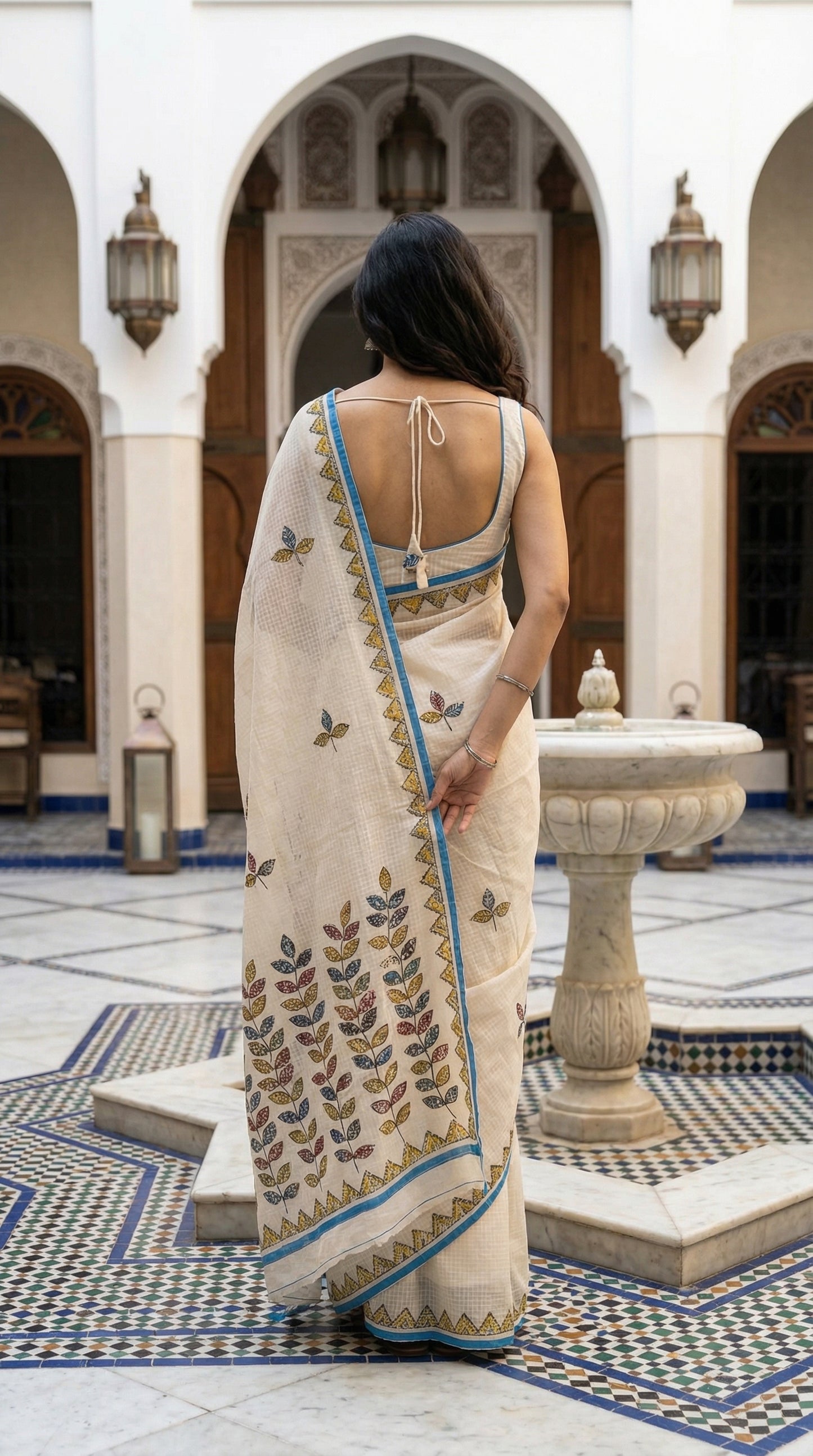 Woman in a white-blue-kota-doria-saree, standing in an ornate courtyard
