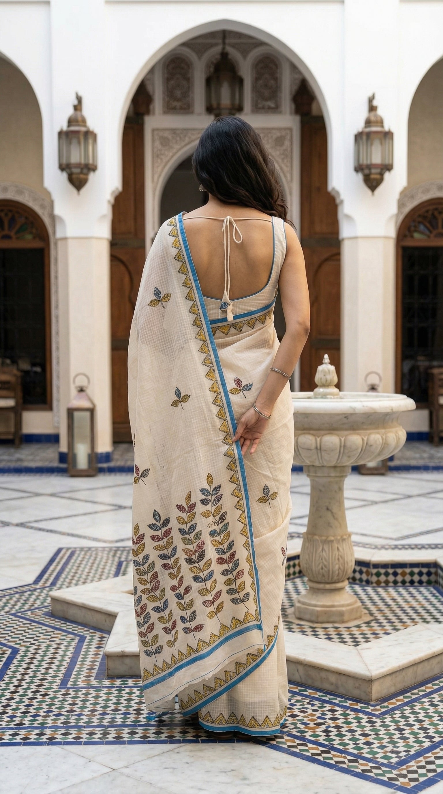 Woman in a white-blue-kota-doria-saree, standing in an ornate courtyard