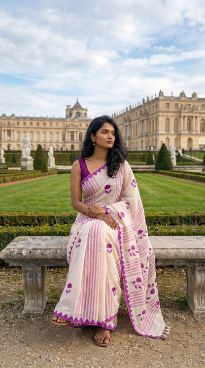 Woman in a white-cotton-saree-magenta-applique, sitting on a bench in front of a grand building.