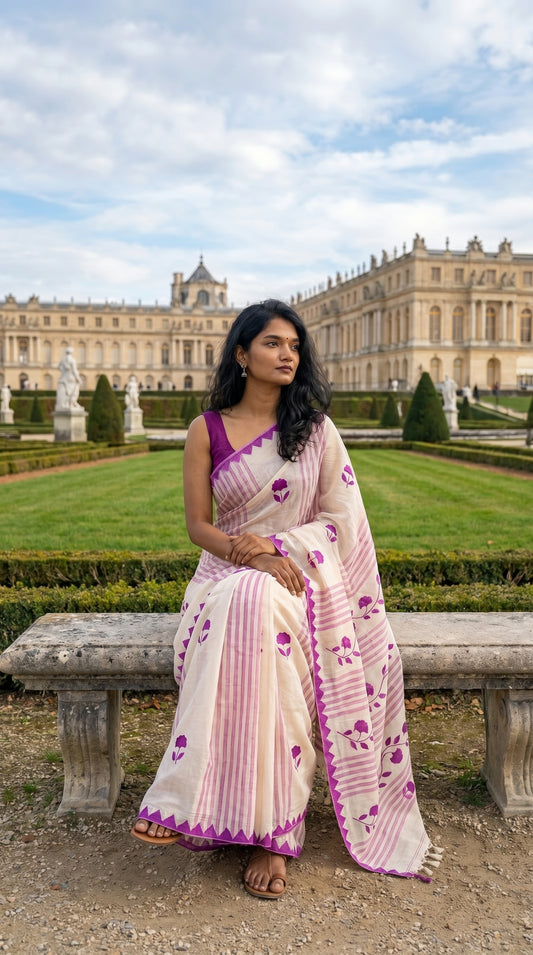 Woman in a white-cotton-saree-magenta-applique, sitting on a bench in front of a grand building.