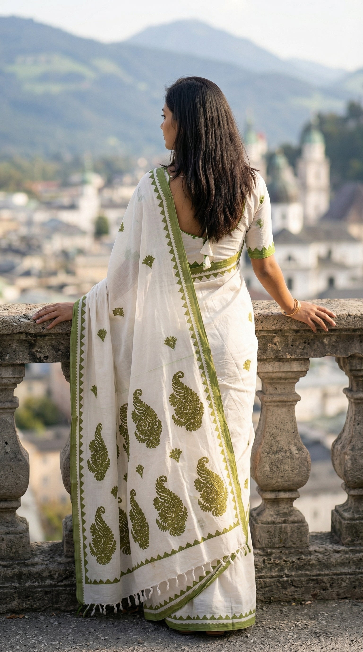 Woman in a white-green-cotton-linen-saree, standing on a balcony overlooking a scenic landscape.