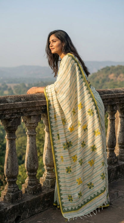 Woman in a white-green-yellow-applique-saree, standing on a balcony with a scenic view