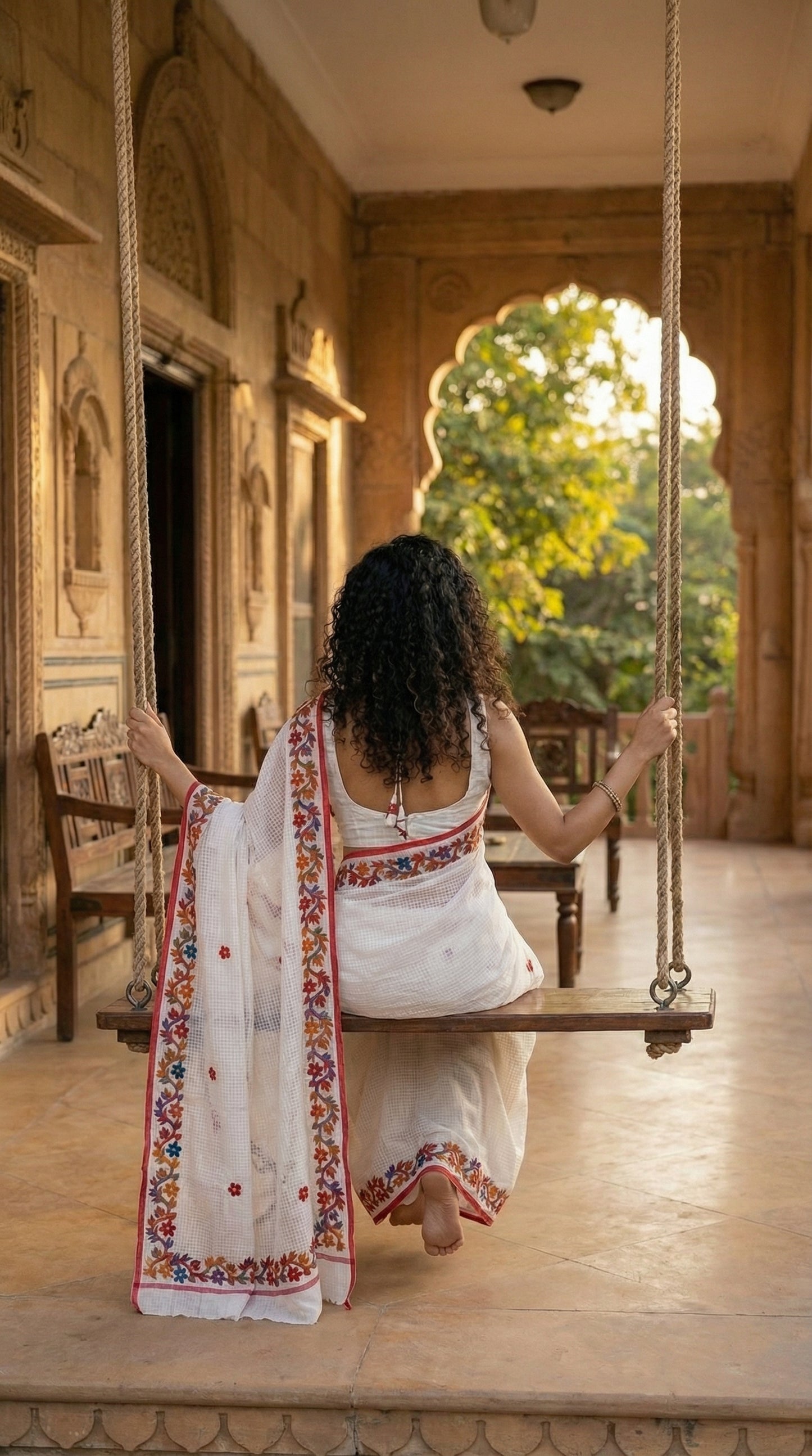 Woman in a white-kota-doria-saree, sitting on a swing with a scenic background