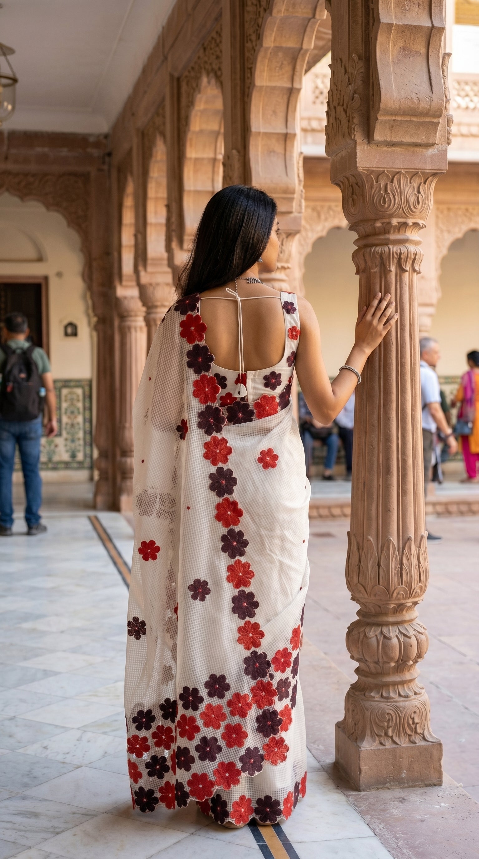 Woman in a white-maroon-brown-mirror-saree, standing in an architectural setting with columns and arches.