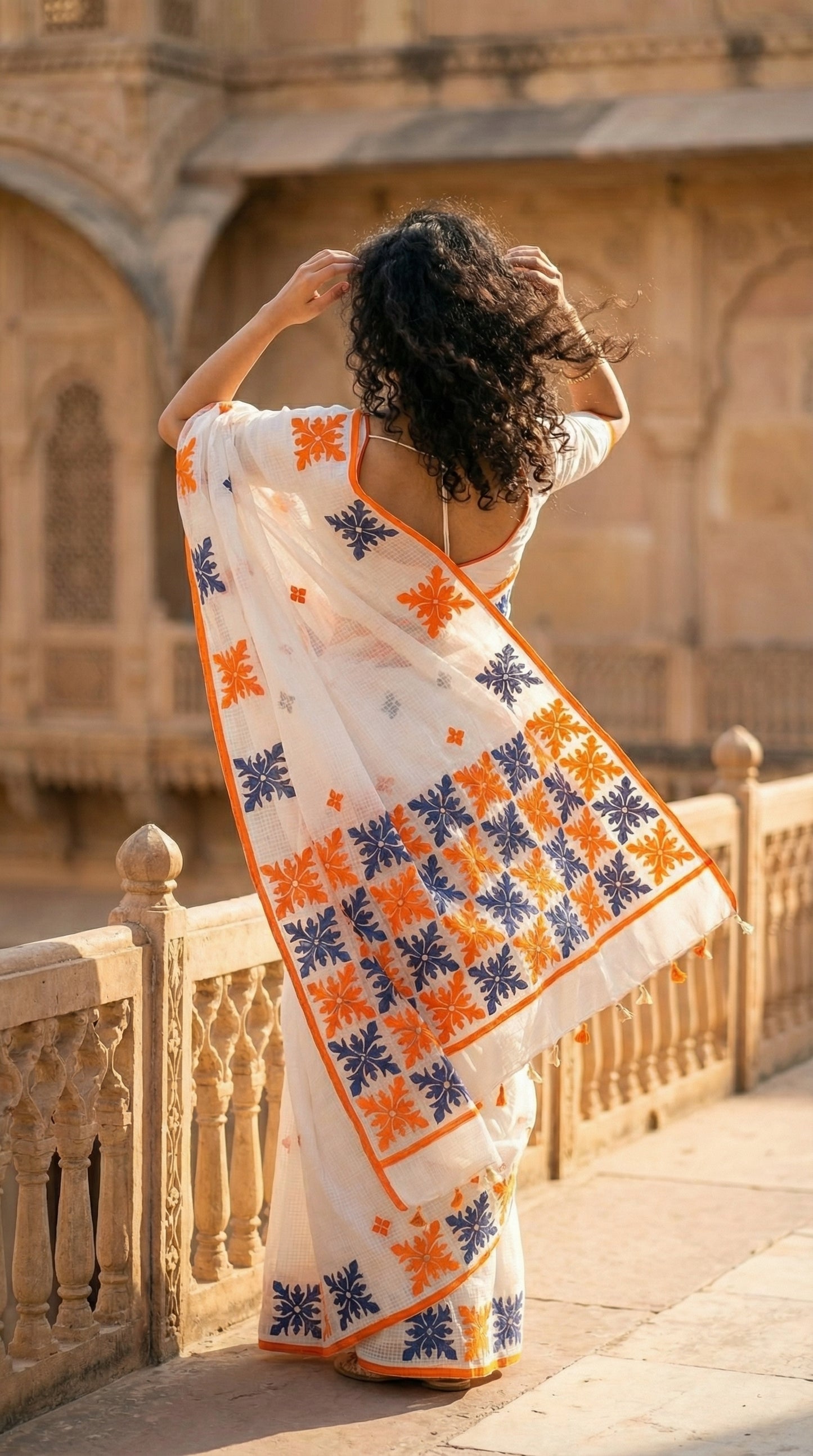 Woman in a white-orange-grey-applique-kota-saree, standing in front of an architectural structure.