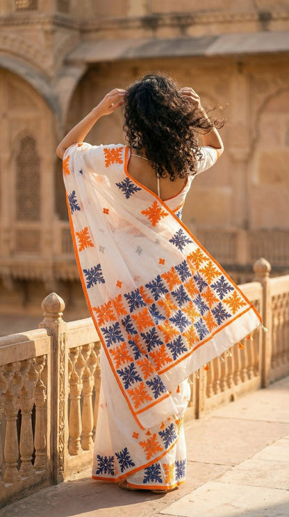 Woman in a white-orange-grey-applique-kota-saree, standing in front of an architectural structure.
