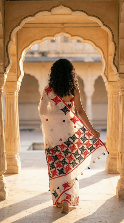 Woman in a white-red-black-applique-kota-saree, against a colorful tiled wall. walking through an archway with a blurred background