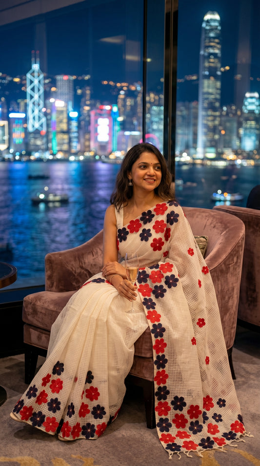 Woman in a white-red-black-mirror-saree, sitting in a chair with a city skyline in the background