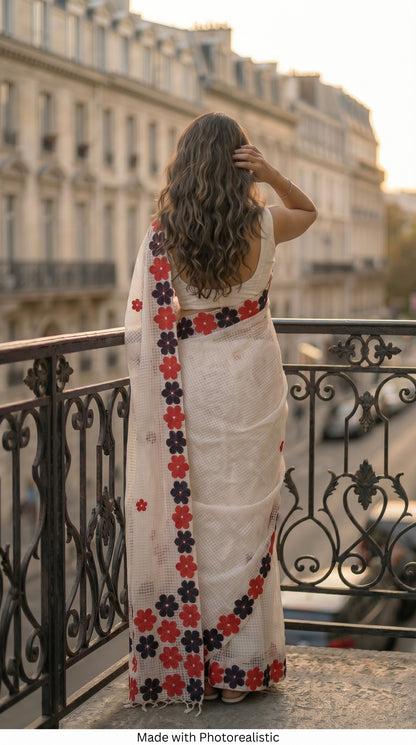 Woman in a white-red-black-mirror-saree, standing on a balcony overlooking a cityscape.