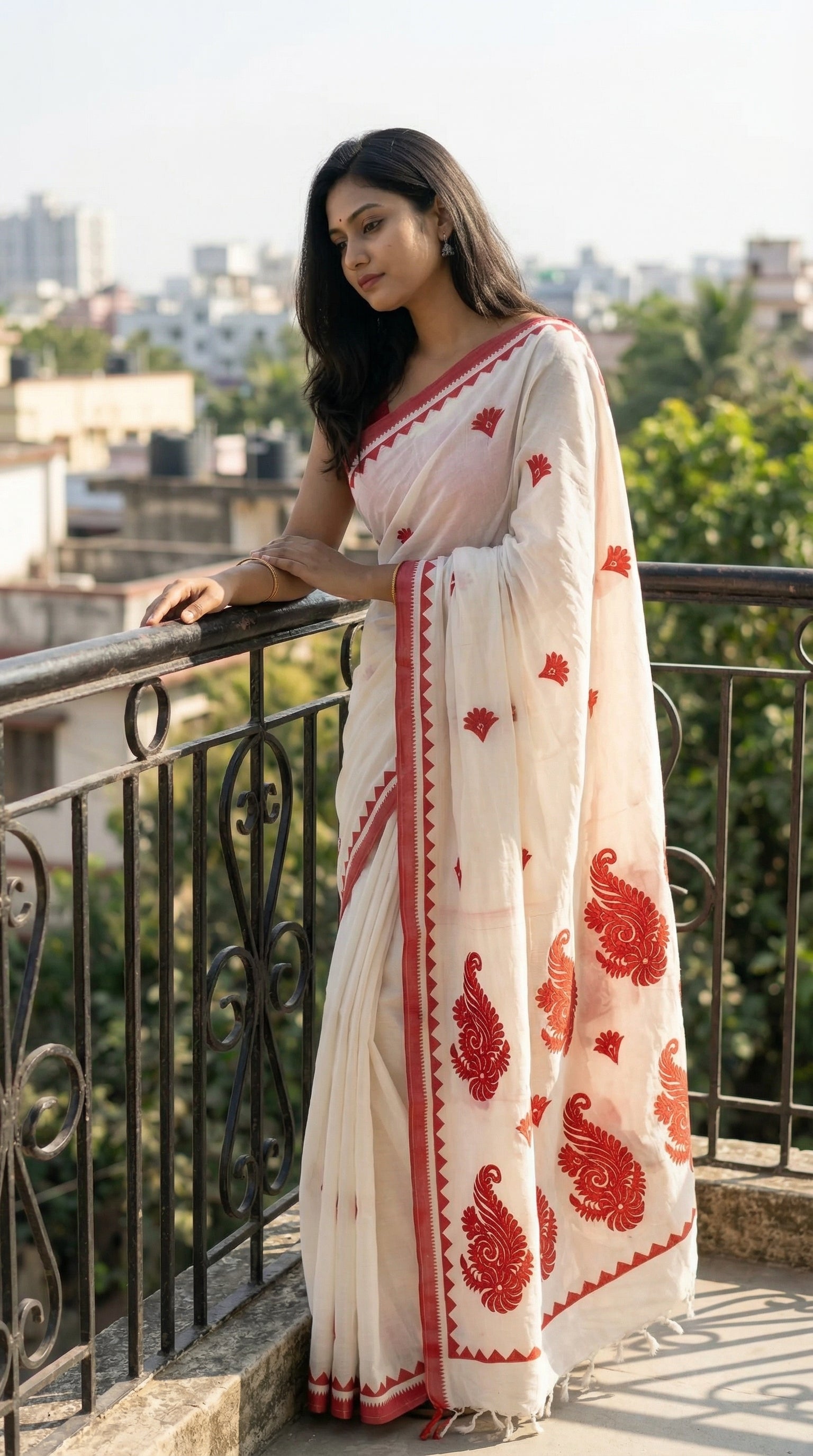 Woman in a white-red-cotton-linen-saree, standing on a balcony with a cityscape background